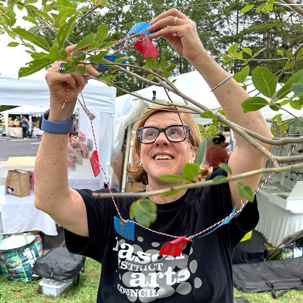 Mary Welch Higgins, seen here hanging tags on a branch, initiated the Mason District Arts Council Wishing Tree project as part of the Mason Arts 250 activities.