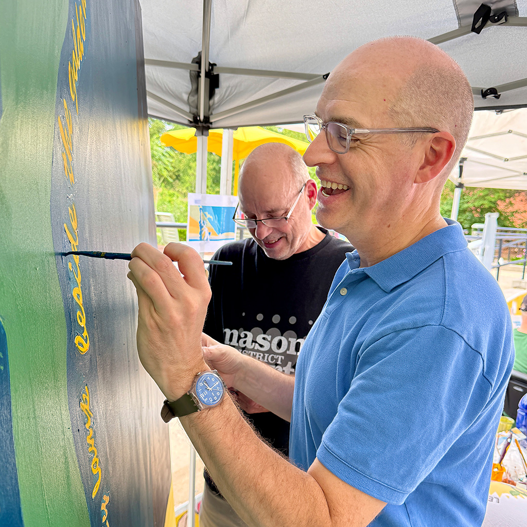 ArtsFairfax President & CEO Stuart Holt (right), joins Mason District Arts Council chair James Albright (center), during the community mural project and Wishing Tree event staged as part of the Mason Arts 250 series of activities to commemorate America's 250 founding anniversary.