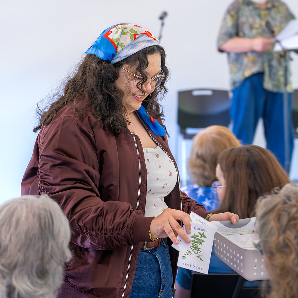 Sibyl Dauer hands out symbolic seeds to audience members during a reading by Anthony Dauer as Thomas Paine in which he asks he asks what we intend to do with our citizen’s inheritance.