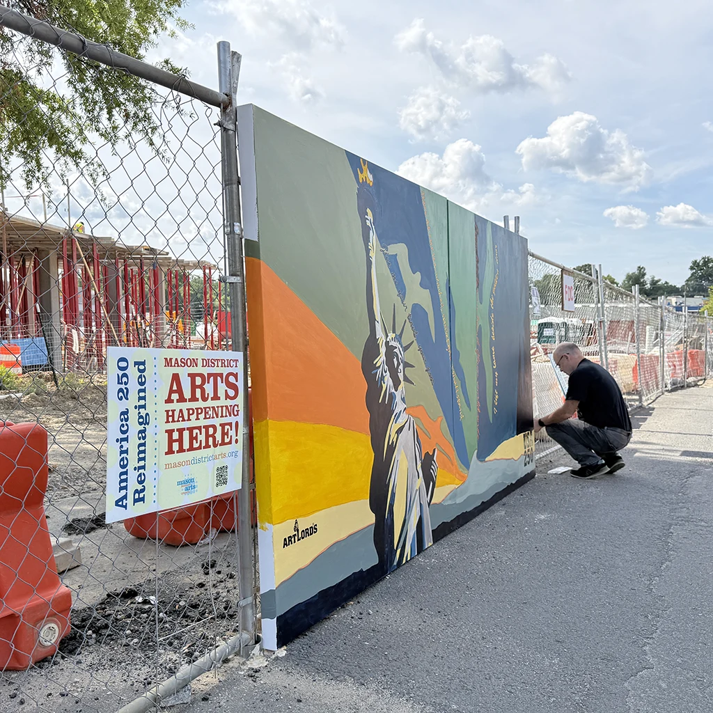 Mason District Arts Council chair, James Albright attaches the community mural created for the Mason Arts 250 project, a community-wide commemoration of the United States Semiquincentennial, onto the construction fencing for the future Eastgate Apartments building in Annandale, Virginia on July 24, 2026.